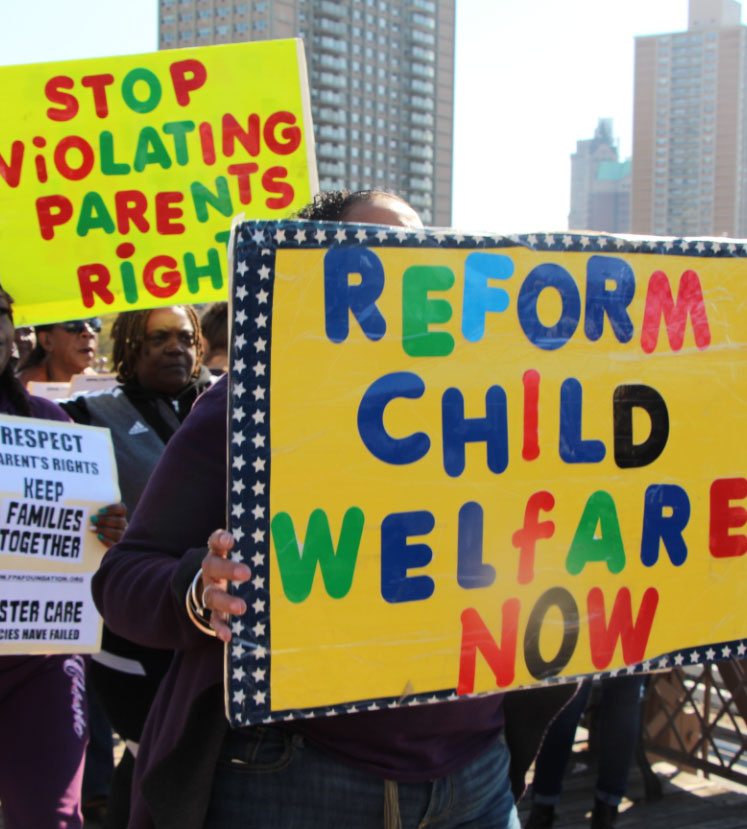 Activists hold protest signs reading 'Reform Child Welfare Now', 'Stop Violating Parents Rights', 'Keep Familes Together'.